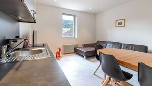 Une cuisine moderne avec un évier en acier inoxydable, un tabouret décoratif rouge et une fenêtre donnant sur un paysage verdoyant.