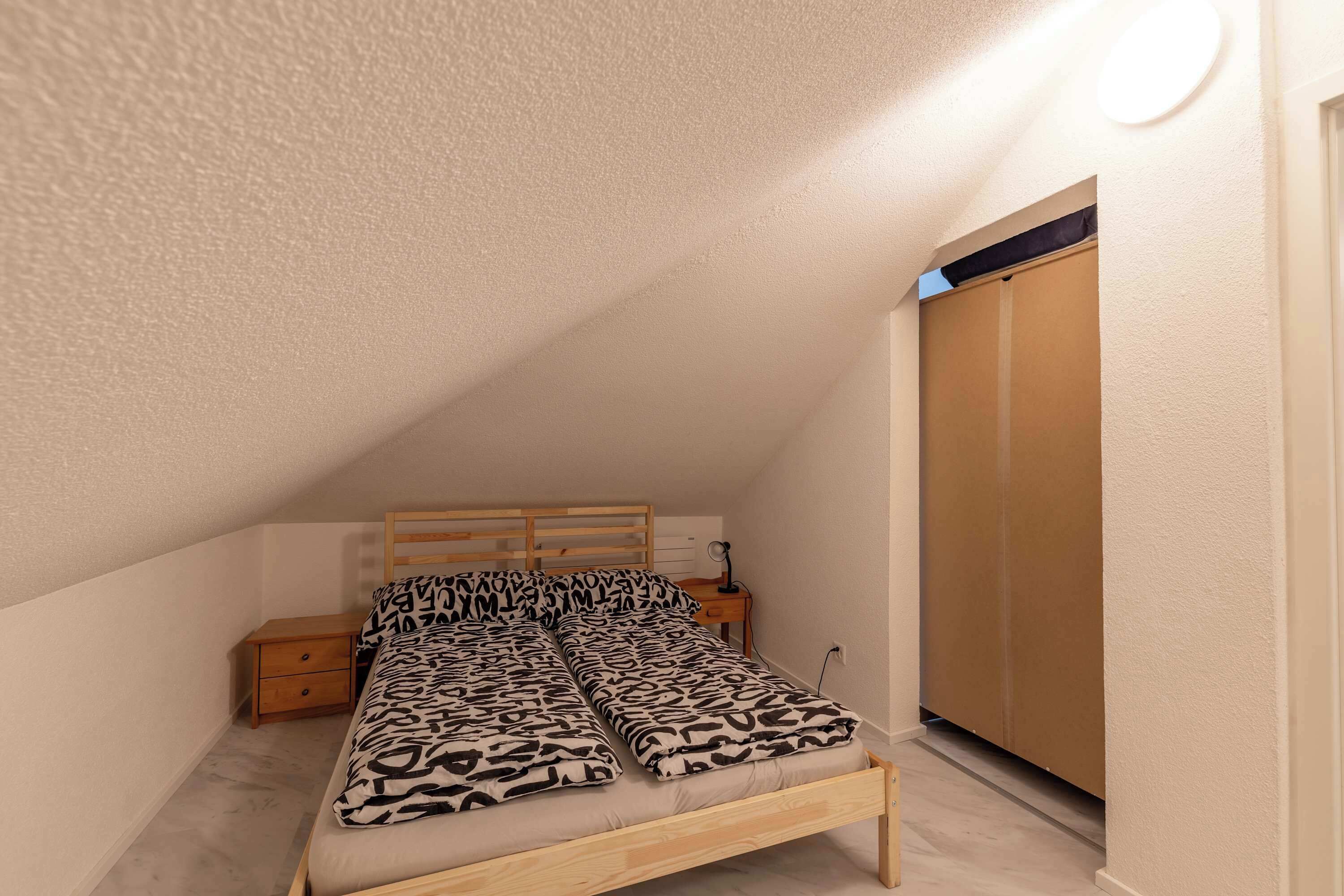 Een slaapkamer met een bed, houten hoofdbord, nachtkastje en een garderobe.