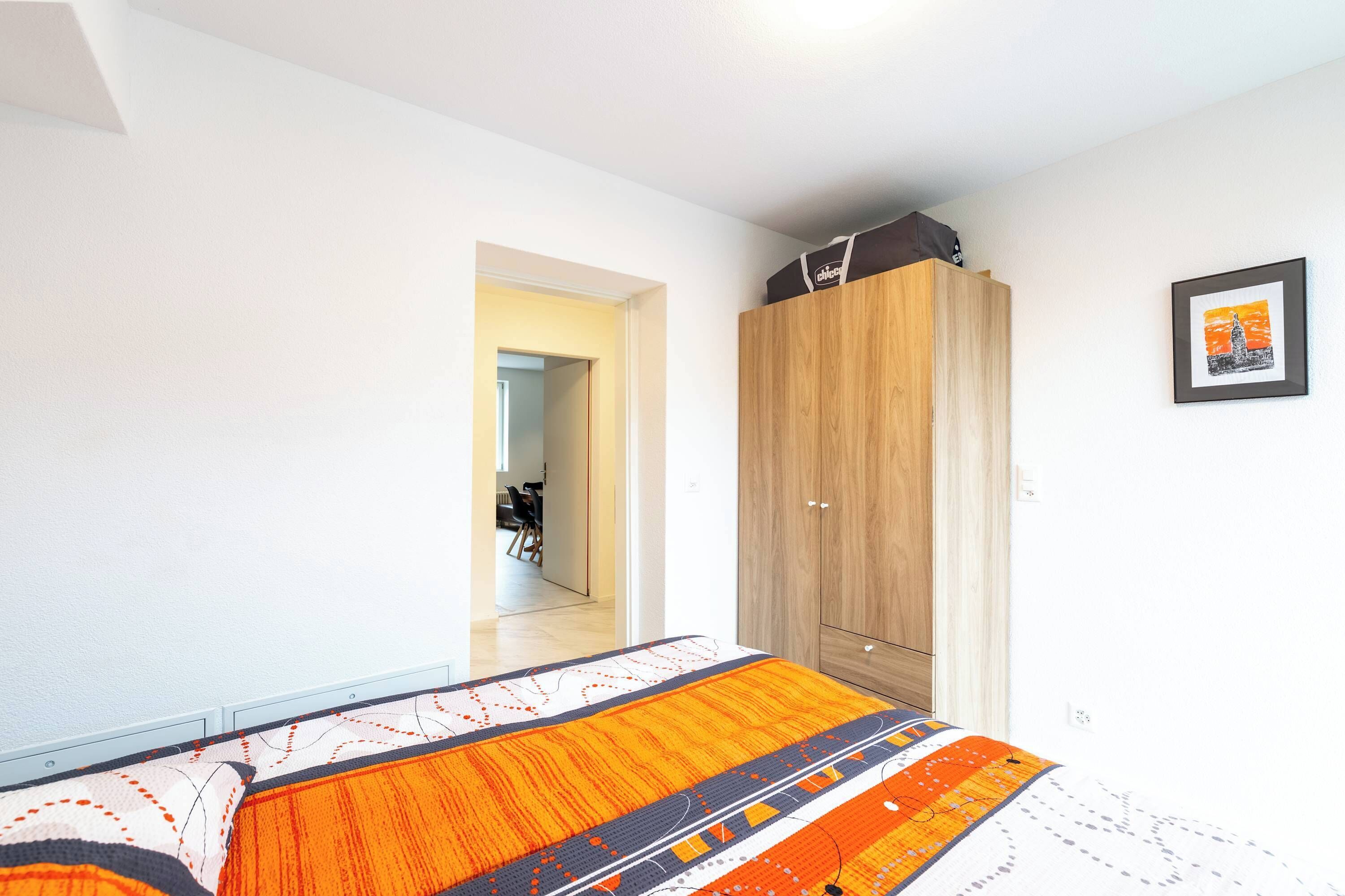 Une chambre à coucher comprenant un lit, une armoire et une porte donnant sur une autre pièce.