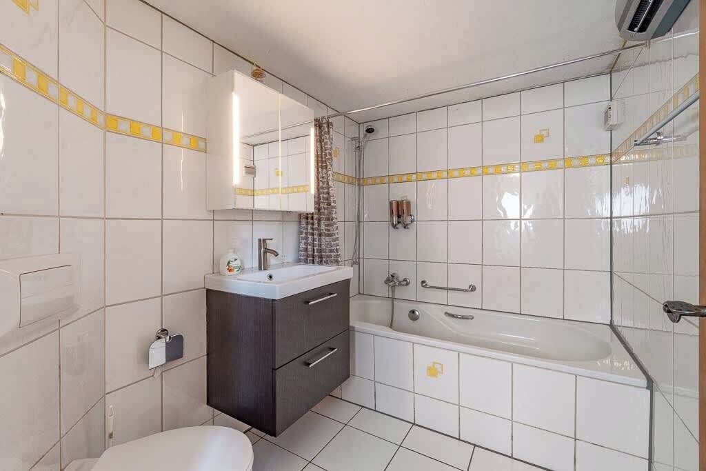 Une salle de bain moderne avec des carreaux blancs, une baignoire, une douche, des toilettes et un meuble-lavabo avec un miroir.