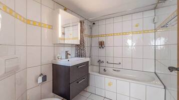 Une salle de bain moderne avec des carreaux blancs, une baignoire, une douche, des toilettes et un meuble-lavabo avec un miroir.