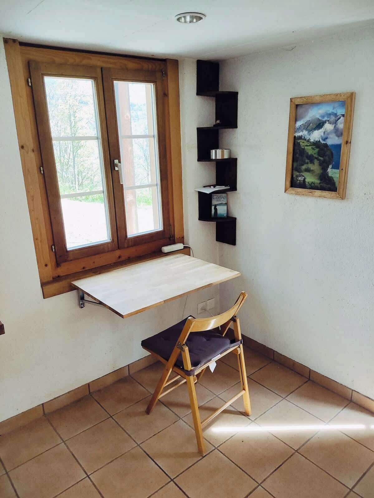 Une pièce comprenant un bureau en bois, une chaise, une fenêtre et une étagère avec divers objets.