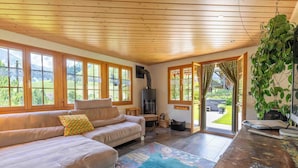 Ein gemütliches Wohnzimmer mit einer Couch, einem Teppich, einem Holztisch und Blick ins Freie durch große Fenster.