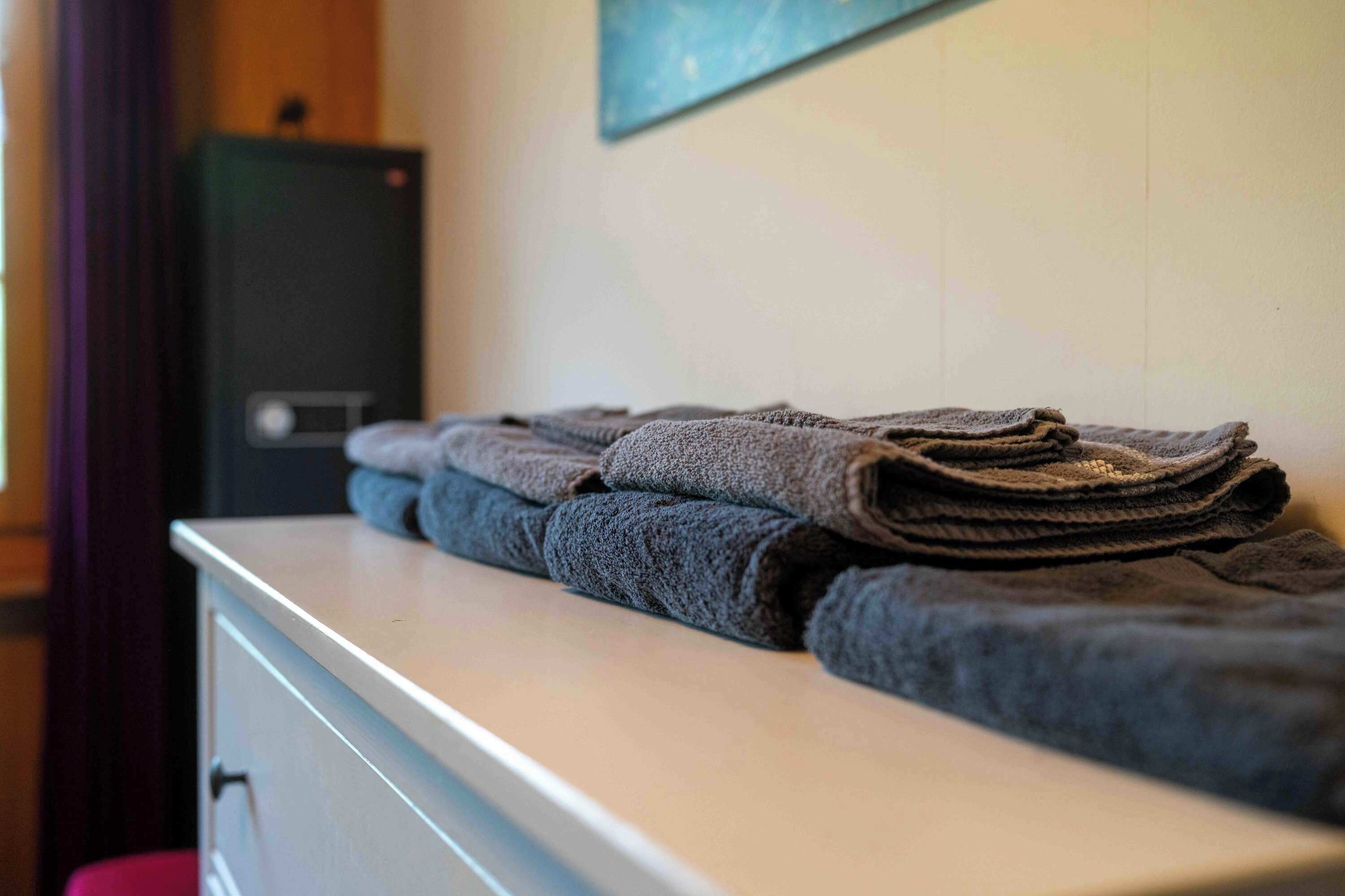 A neatly folded stack of towels on a white counter in a room with a wooden cabinet and a painting on the wall.