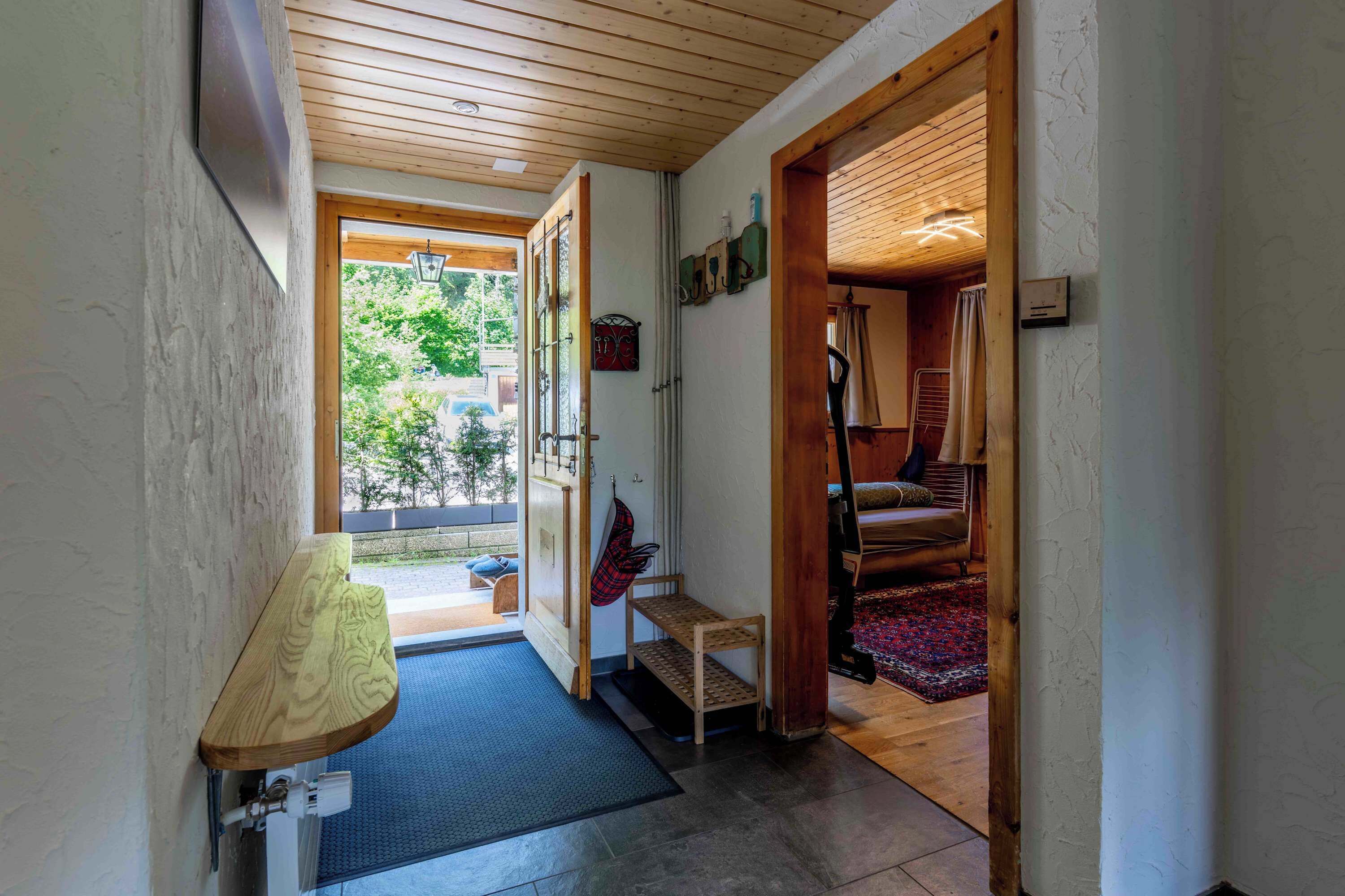 Un corridoio con una panca di legno, un tavolino e una porta che dà su una stanza con una sedia e un tappeto.