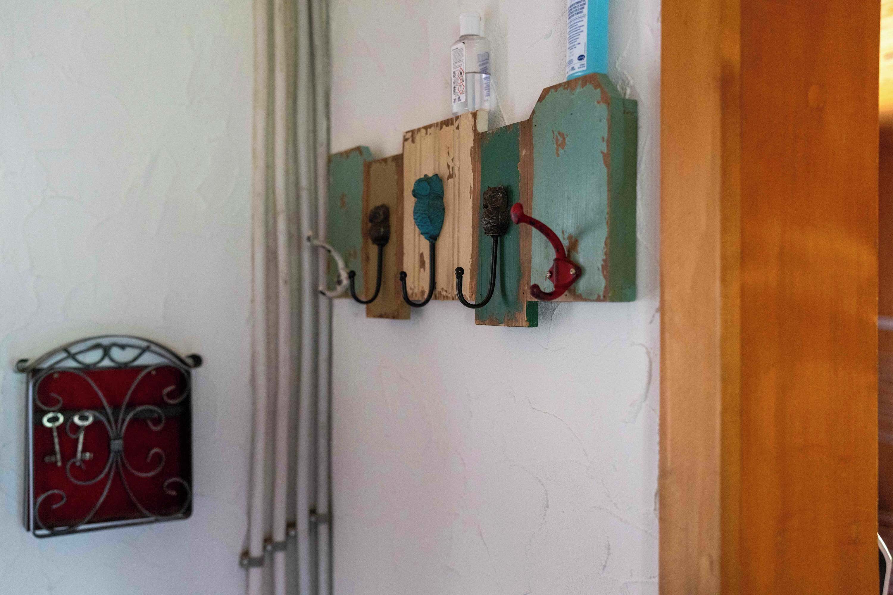 Un porte-objets en bois fixé au mur, muni de crochets, un petit porte-clés en métal et une bouteille blanche.