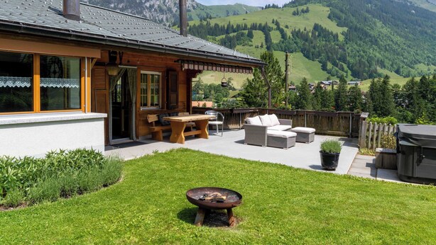 Ein Holzhaus mit Terrasse, Sitzgelegenheiten im Freien und einem Feuerkorb.