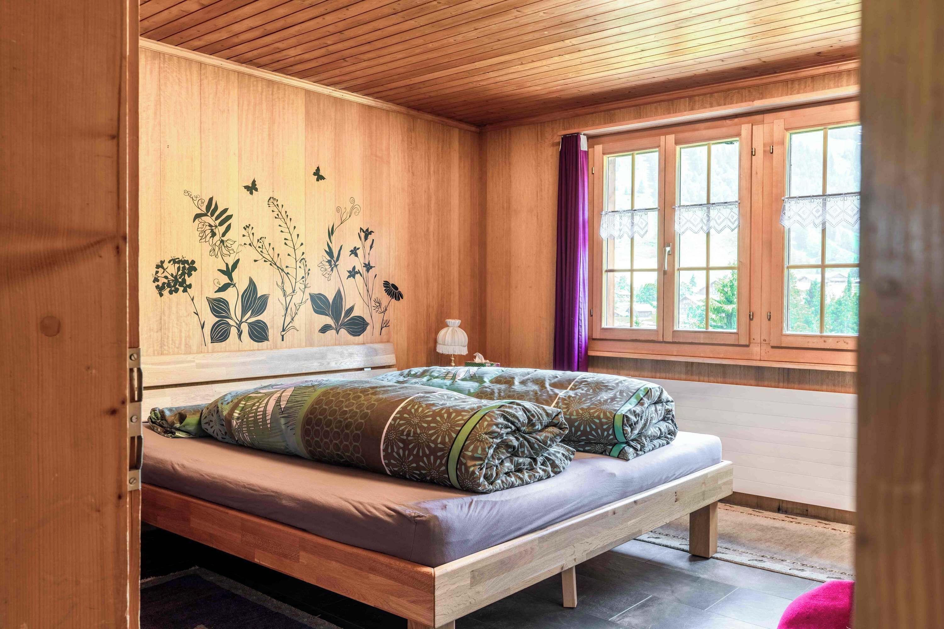 Une pièce en bois avec un lit, une fenêtre avec des rideaux et un mur décoré d’œuvres d’art florales.