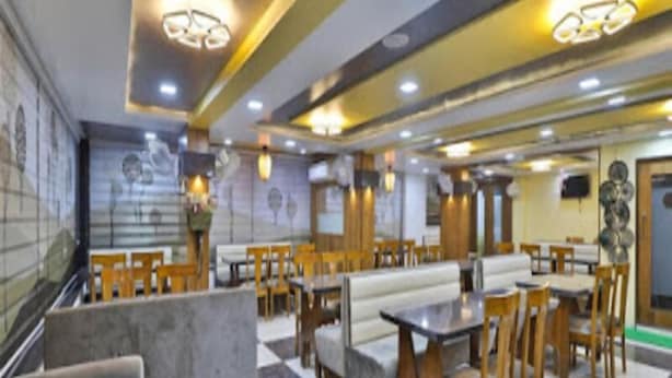 A spacious restaurant with high ceilings, modern lighting, and a mix of seating including tables and booths. - Hotel Krishna Palace (Becharaji)