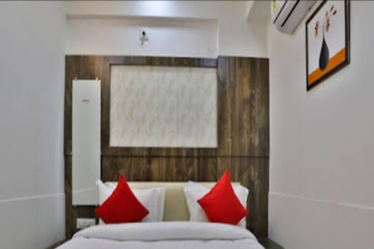 A hotel room with a bed, a wooden headboard, and a wall-mounted air conditioning unit.