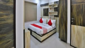 A bedroom with a bed, a ceiling fan, and wooden doors. - Hotel Krishna Palace (Becharaji)