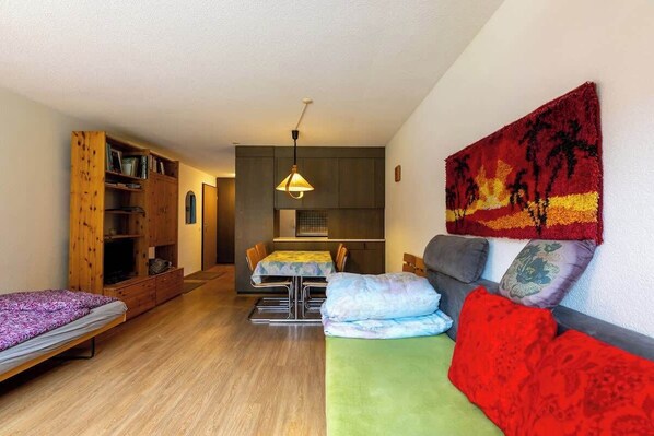 A compact living space with a sofa, a bed, a dining area, and a kitchenette.