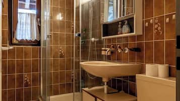 A bathroom with a glass-enclosed shower, a sink, a toilet, and a mirror above the sink.