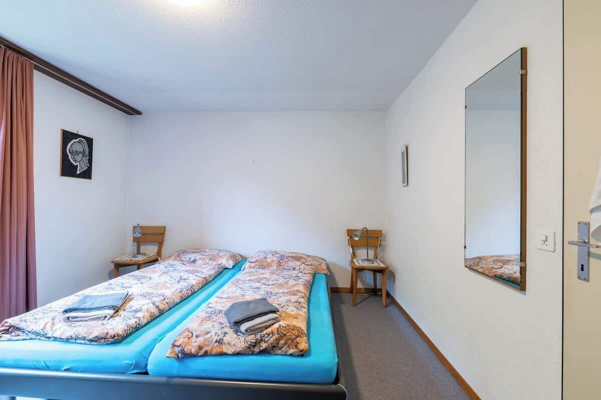 A room with two beds, a mirror, a chair, and a picture on the wall.