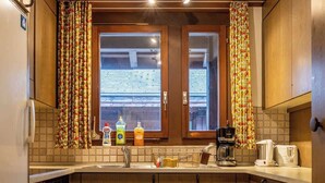 Eine kleine Küche mit Holzschränken, einer gefliesten Spritzschutzwand und einem Fenster mit Vorhängen.