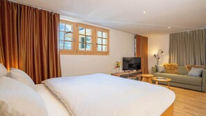 A hotel room with a large bed, a television, a sofa, and a small table. - Mountain View Studio Adelboden|Gondola & Spa (Adelboden)