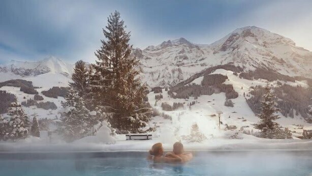 A hot spring with two people in the water, surrounded by snow-covered mountains and a large evergreen tree. - Mountain View Studio Adelboden|Gondola & Spa (Adelboden)