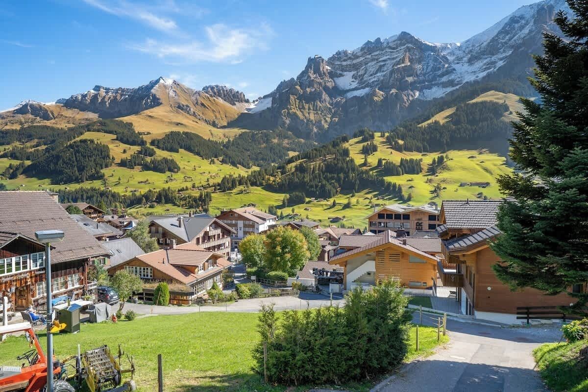 Un village de montagne aux maisons traditionnelles en bois, avec une route dégagée et une vue sur des sommets enneigés.
