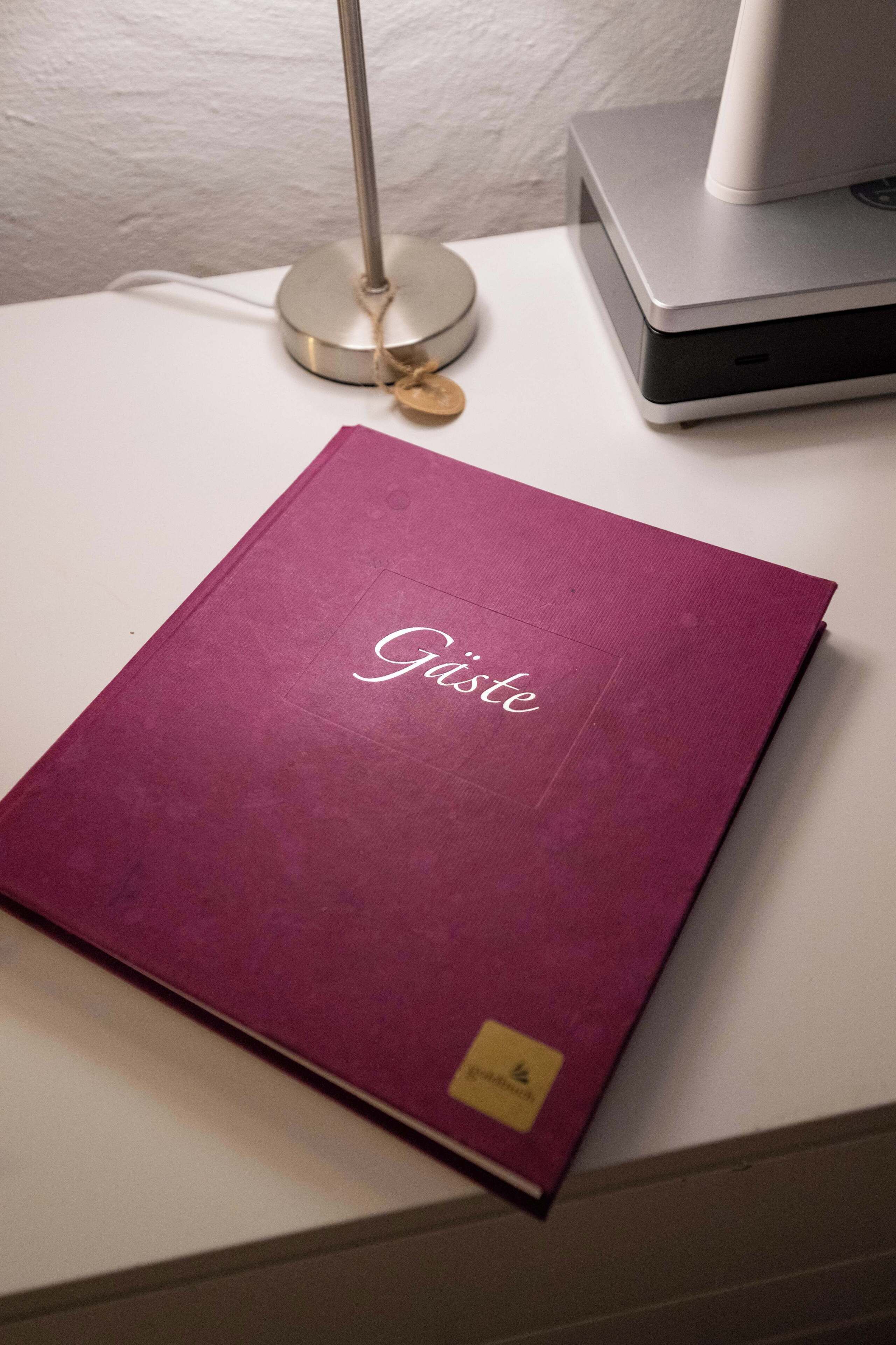 A purple folder with "Gisette" written on it, placed on a white surface next to a lamp and a laptop.