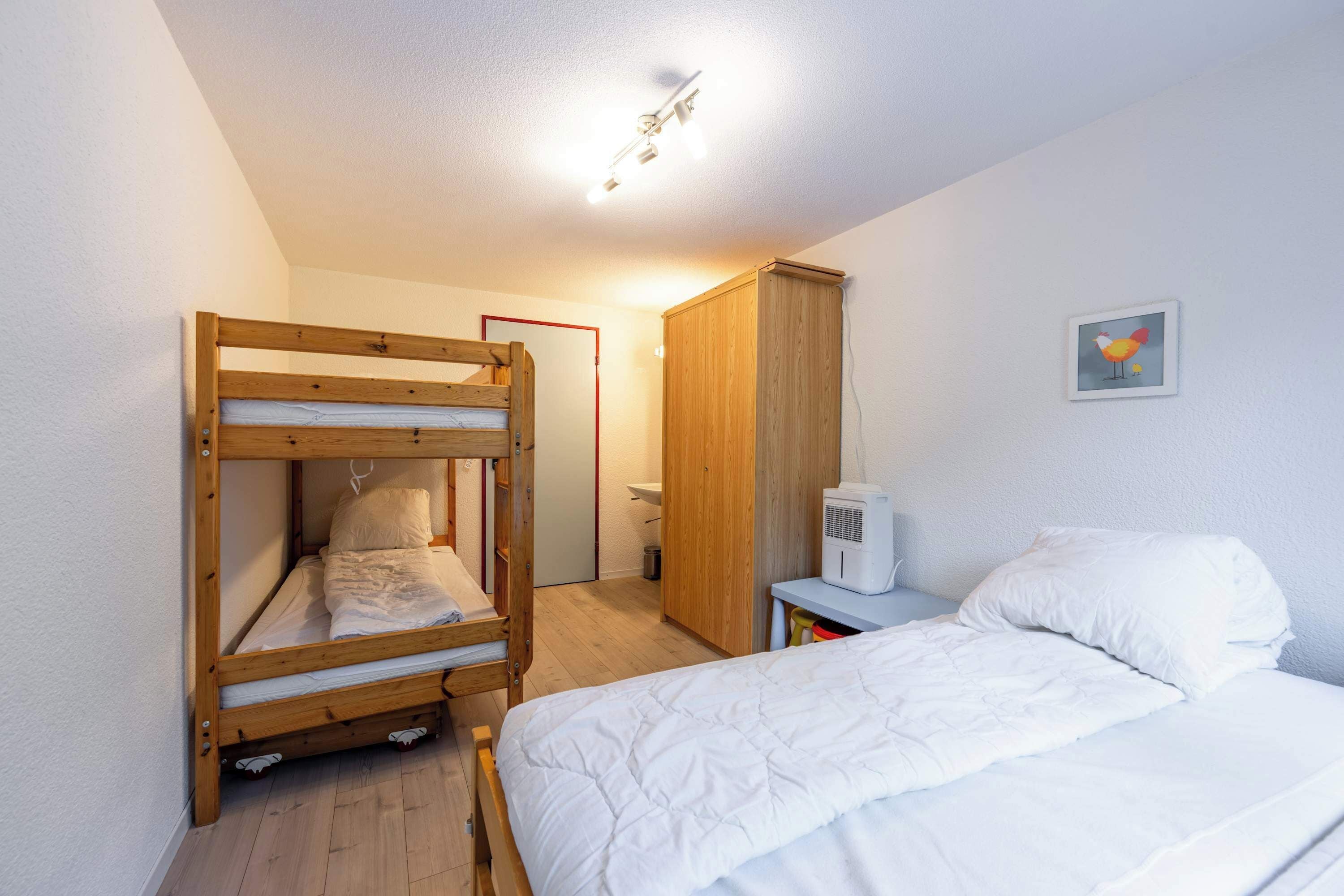 Une chambre comprenant un lit superposé, un lit simple, une armoire, une table de chevet et un radiateur fixé au mur.