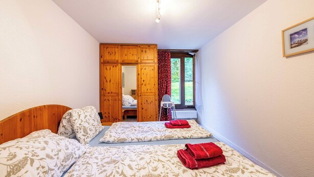 Une chambre avec deux lits, une armoire en bois et une fenêtre avec des rideaux.
