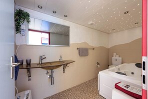 A bathroom with a wooden sink, a large mirror, a towel rack, a bathtub, and a toilet. - Large apartment in the vacation center | Hot Tub (Diemtigen)