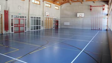 An indoor basketball court with multiple hoops, a red door, and a window.