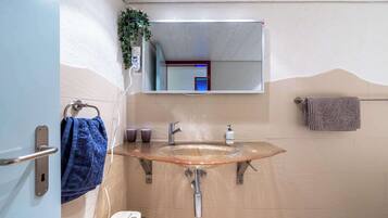 Een badkamer met een glazen wastafel, een handdoekhouder, een spiegel en een plant.