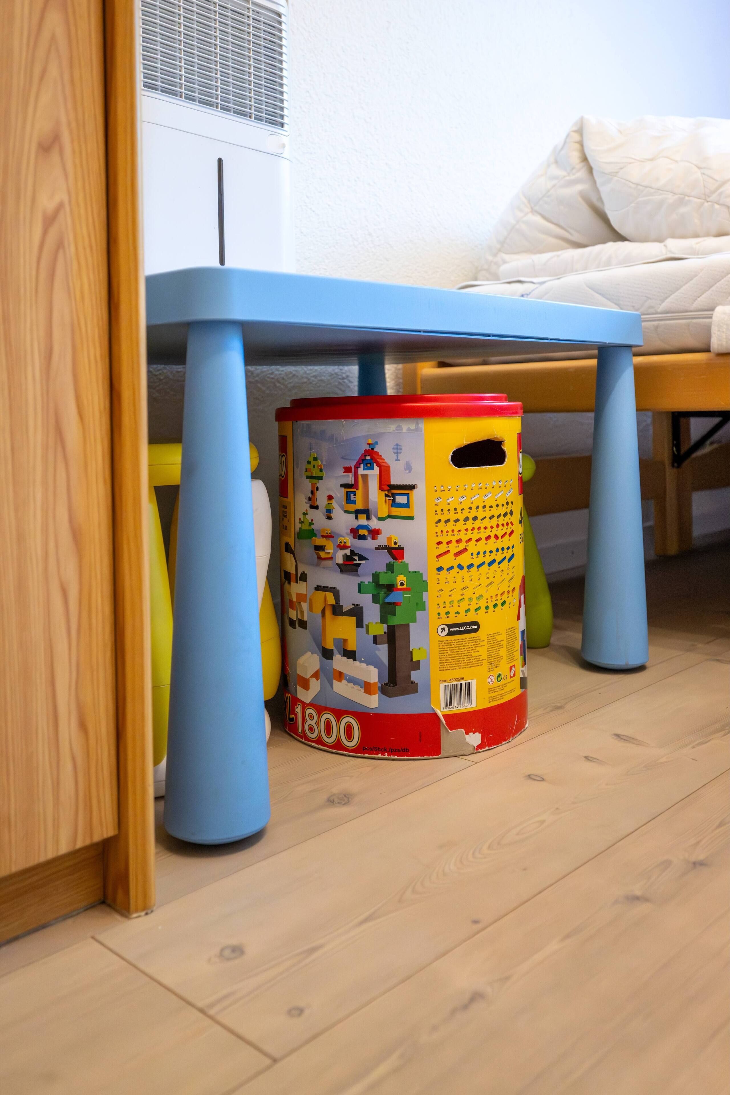 Un'area giochi per bambini con un tavolo blu, un contenitore colorato e un letto bianco.