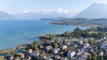 Une vue aérienne d’une ville située au bord d’un lac, avec des immeubles résidentiels, des bateaux sur le lac et des montagnes en arrière-plan.