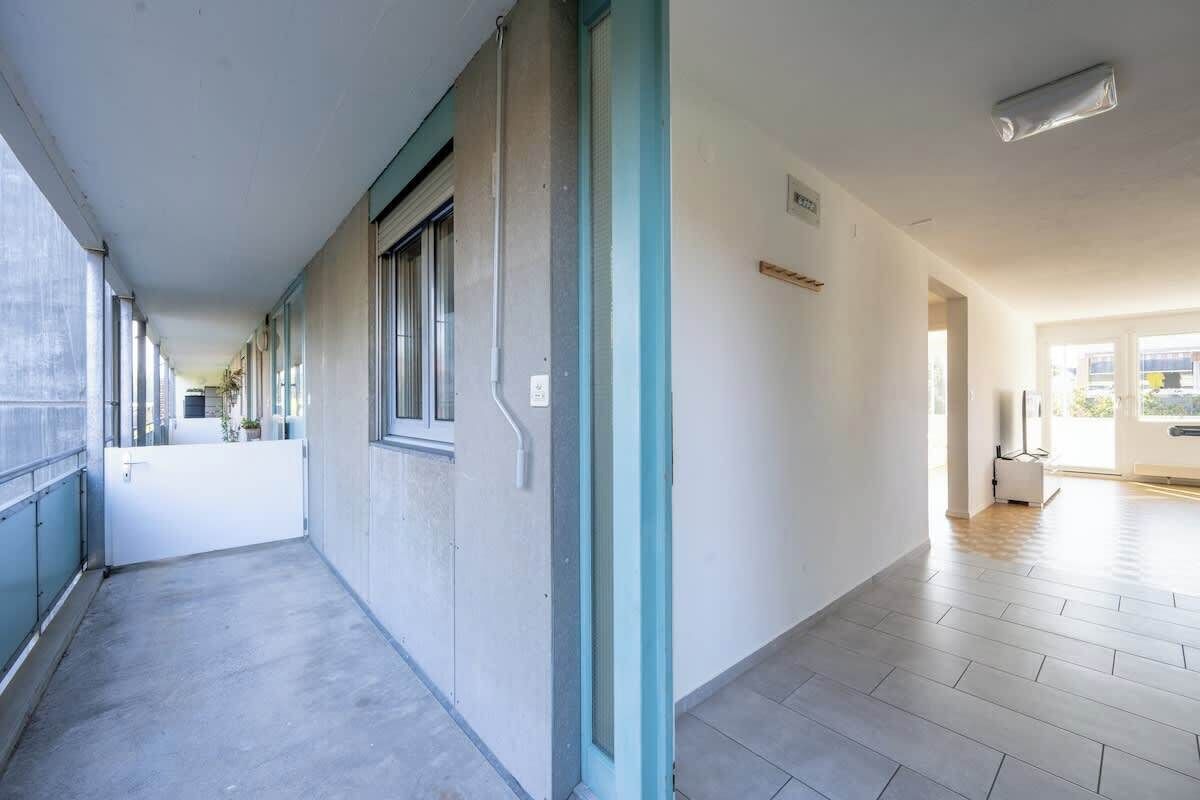 Pitkä, kapea käytävä, jonka lattia on laatoitettu. Vasemmalla puolella on valkoinen ovi ja oikealla puolella ikkuna.