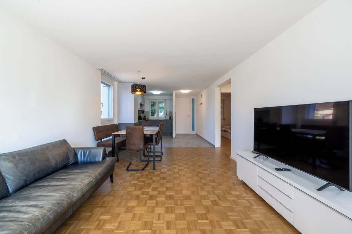 Ein modernes Wohnzimmer mit einer Couch, einem Esstisch, Stühlen und einem Fernseher.