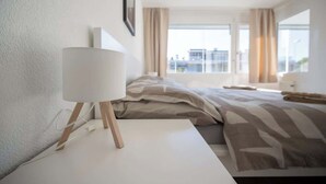 Ett modernt hotellrum med en stor säng, ett sängbord med en lampa och utsikt över staden genom stora fönster.