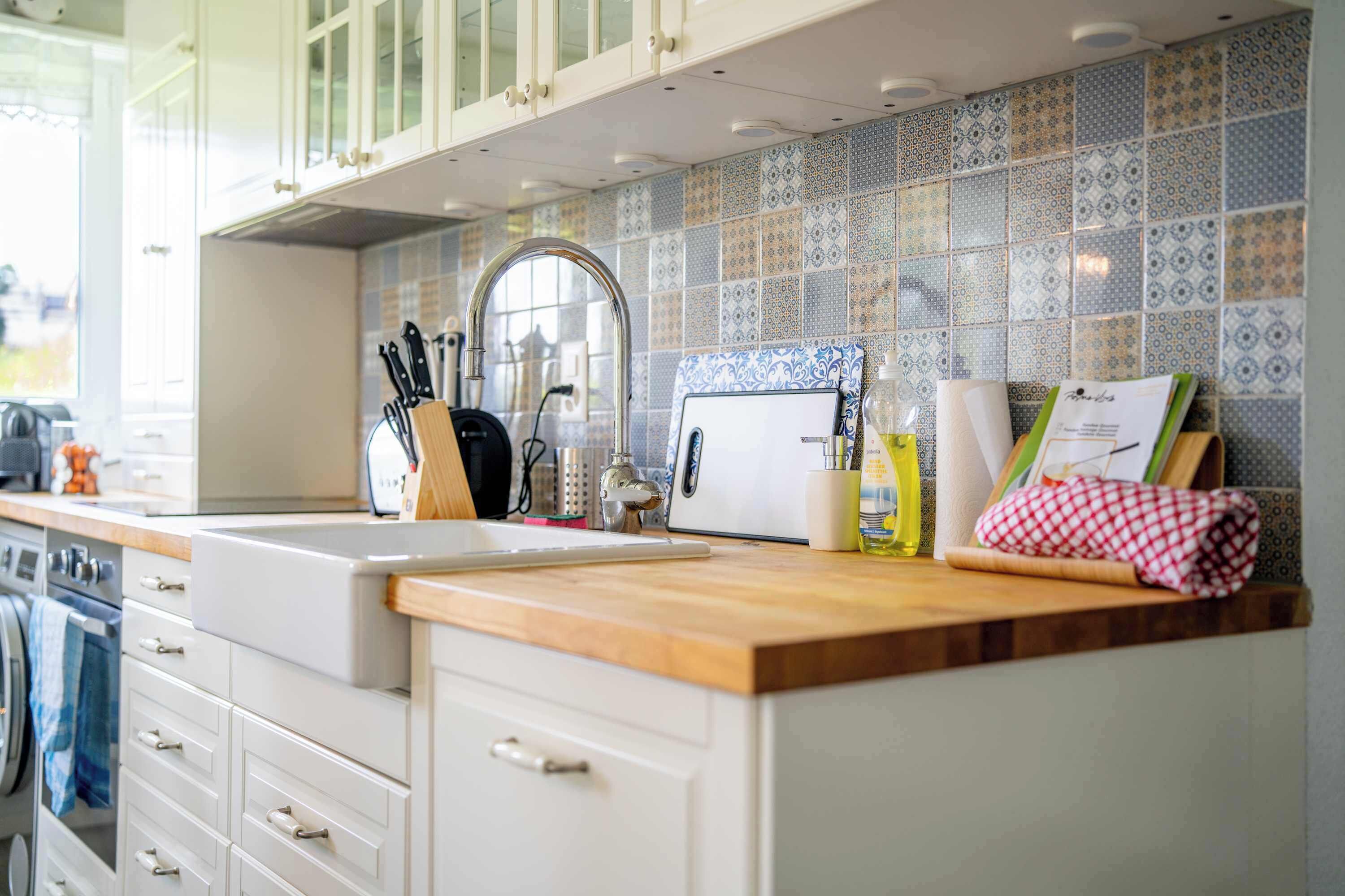 A kitchen with a wooden countertop, white cabinets, a tiled backsplash, and various kitchen utensils.