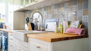 A kitchen with a wooden countertop, white cabinets, a tiled backsplash, and various kitchen utensils.