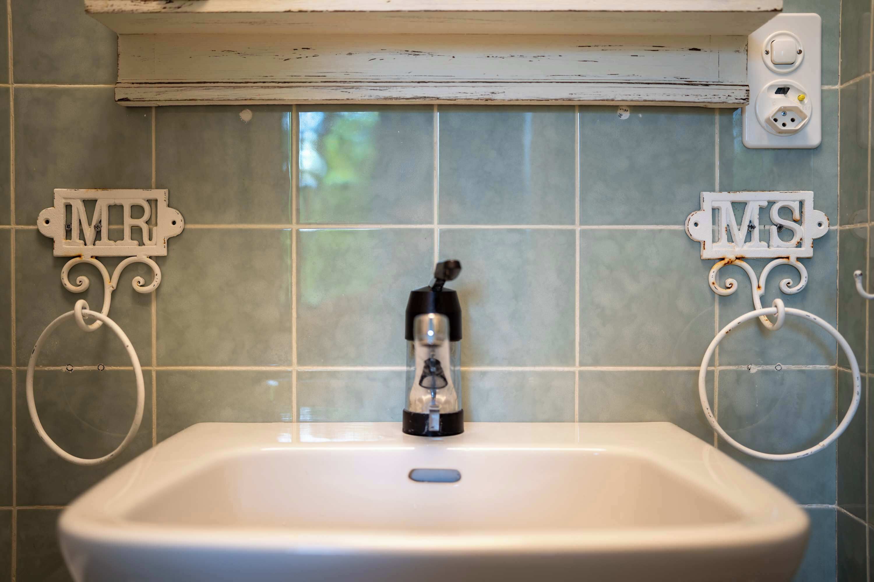 A bathroom with a sink, two towel rings labeled "MR" and "MS," and a faucet.