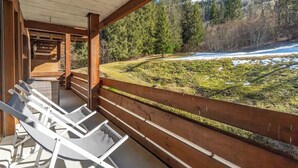 Una terraza de madera con sillones blancos que da vista a un paisaje nevado con árboles y una colina al fondo.