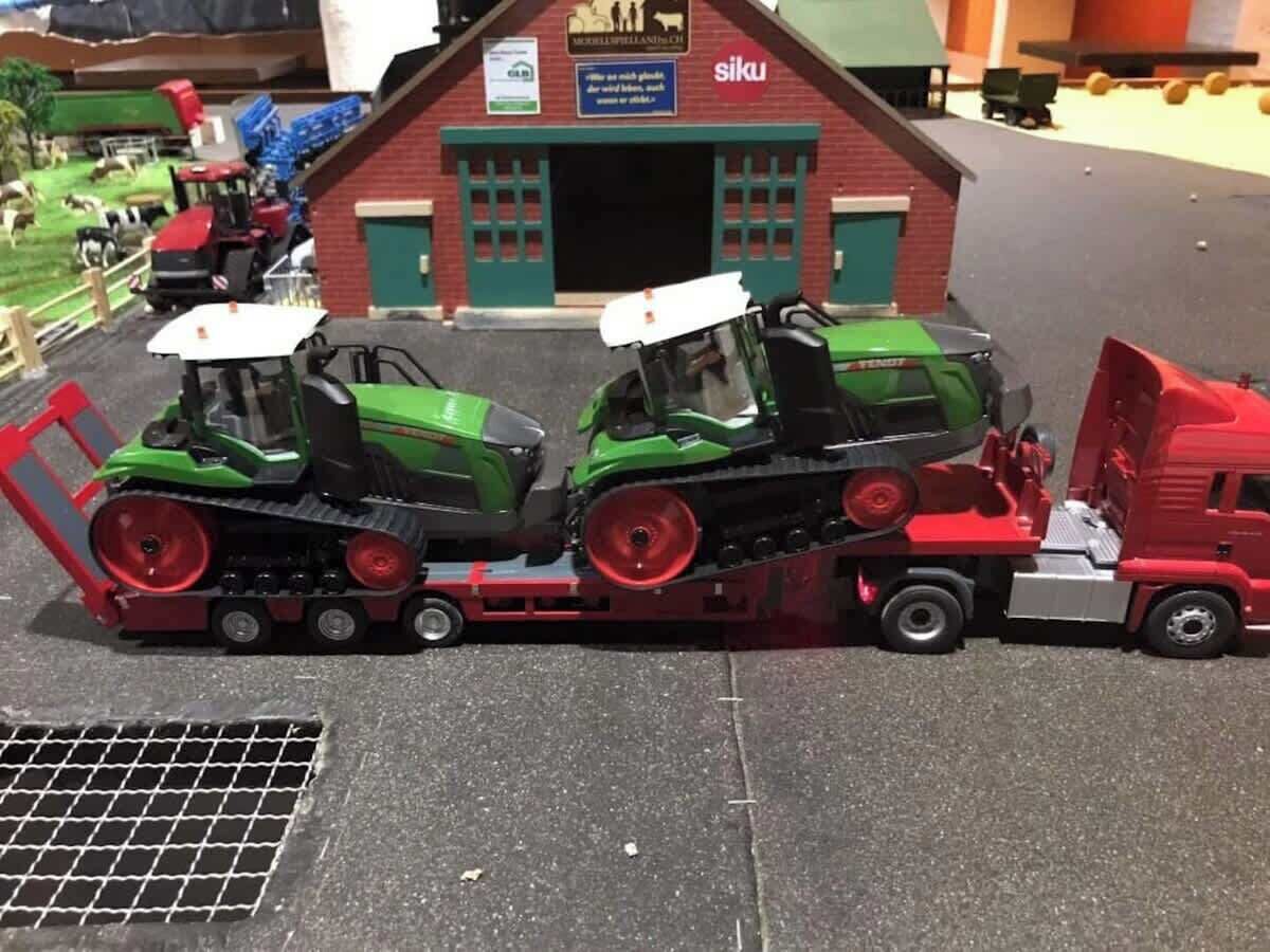 Une maquette de ferme avec deux tracteurs verts et un camion rouge garés devant un bâtiment sur lequel est apposée une enseigne indiquant « siku ».