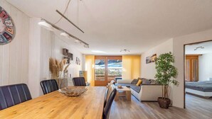 Una sala de estar moderna con una mesa de comedor de madera, sillas negras, un sofá y un ventanal con vistas al exterior.