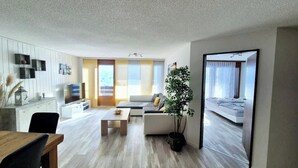 Una sala moderna con un sofá, una mesa de centro y un televisor. Hay un comedor con una mesa y sillas.