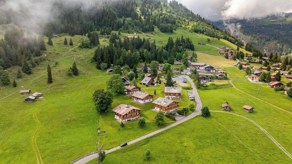 Eine Vogelperspektive auf ein ländliches Dorf mit traditionellen Holzhäusern, einer kurvenreichen Straße und umgebender Natur.