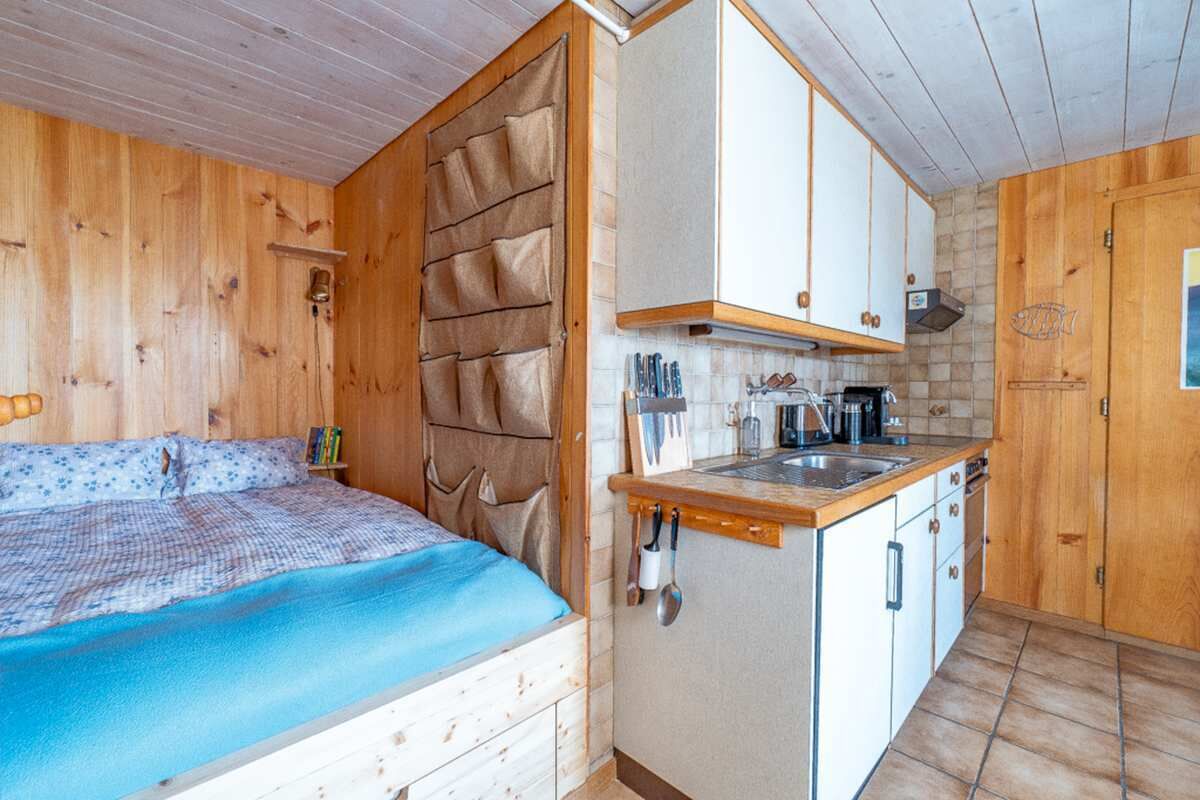 Een kleine kamer met een bed, kitchenette en een houten deur.