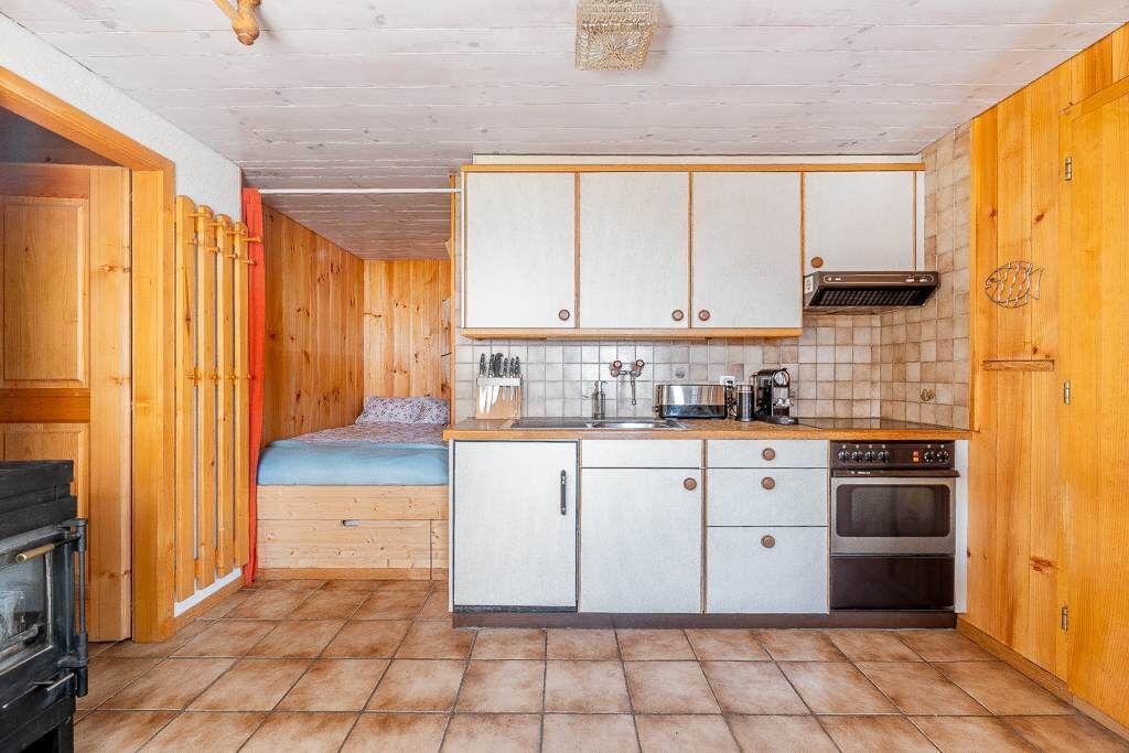 Una cocina compacta con armarios de madera, horno empotrado y un pequeño comedor con banco.