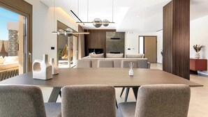 A modern dining area with a long table, multiple chairs, and a hanging light fixture. - Welcome to Ruby Paradise, a luxurious villa nestled in thearea of Sgourou. (Sgourou)