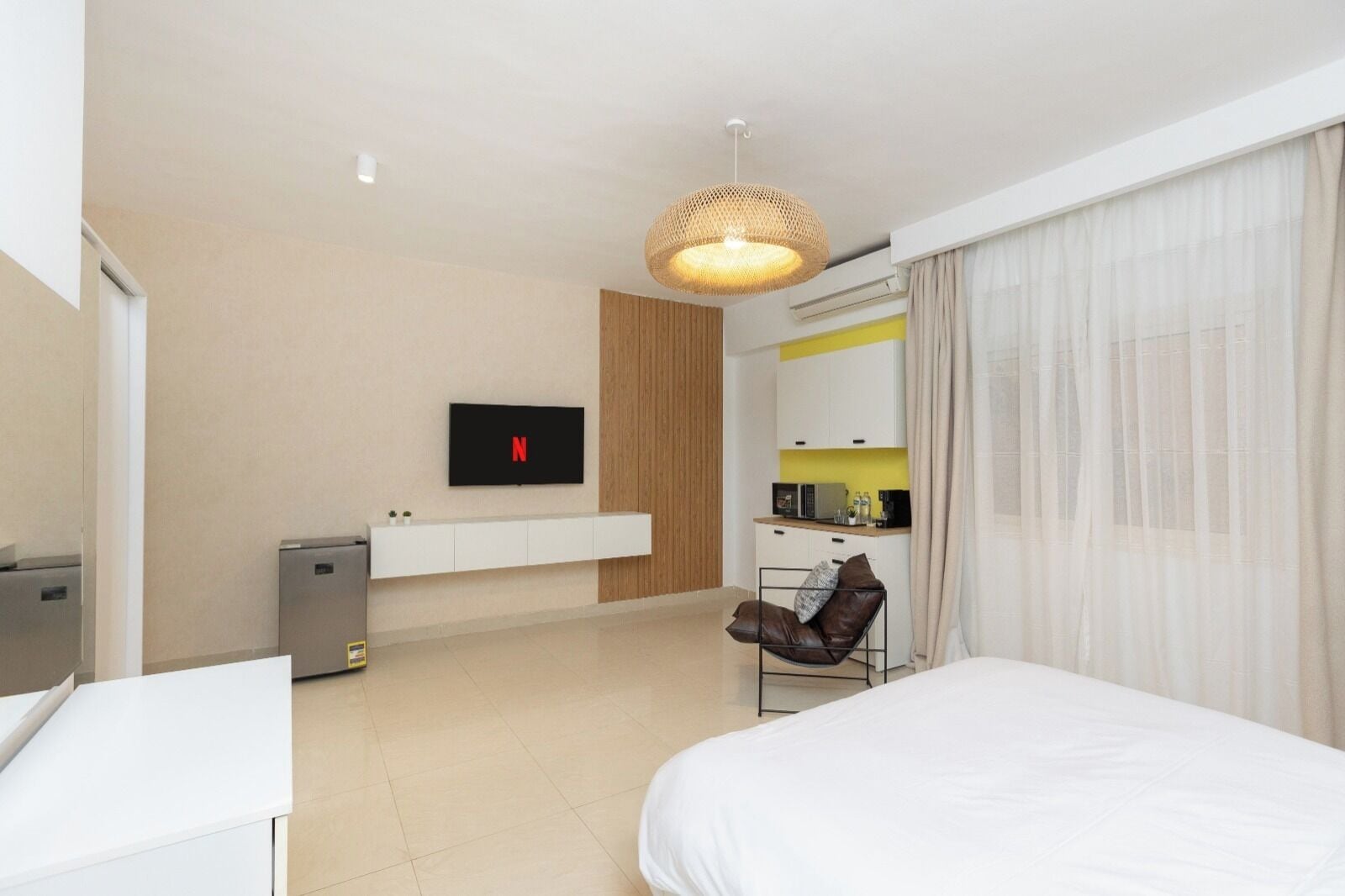 Una camera d'albergo moderna con un letto, una scrivania, una TV a parete, un angolo cottura e un'area salotto con una poltrona.