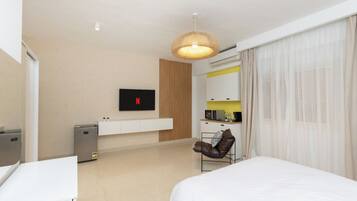 Una camera d'albergo moderna con un letto, una scrivania, una TV a parete, un angolo cottura e un'area salotto con una poltrona.