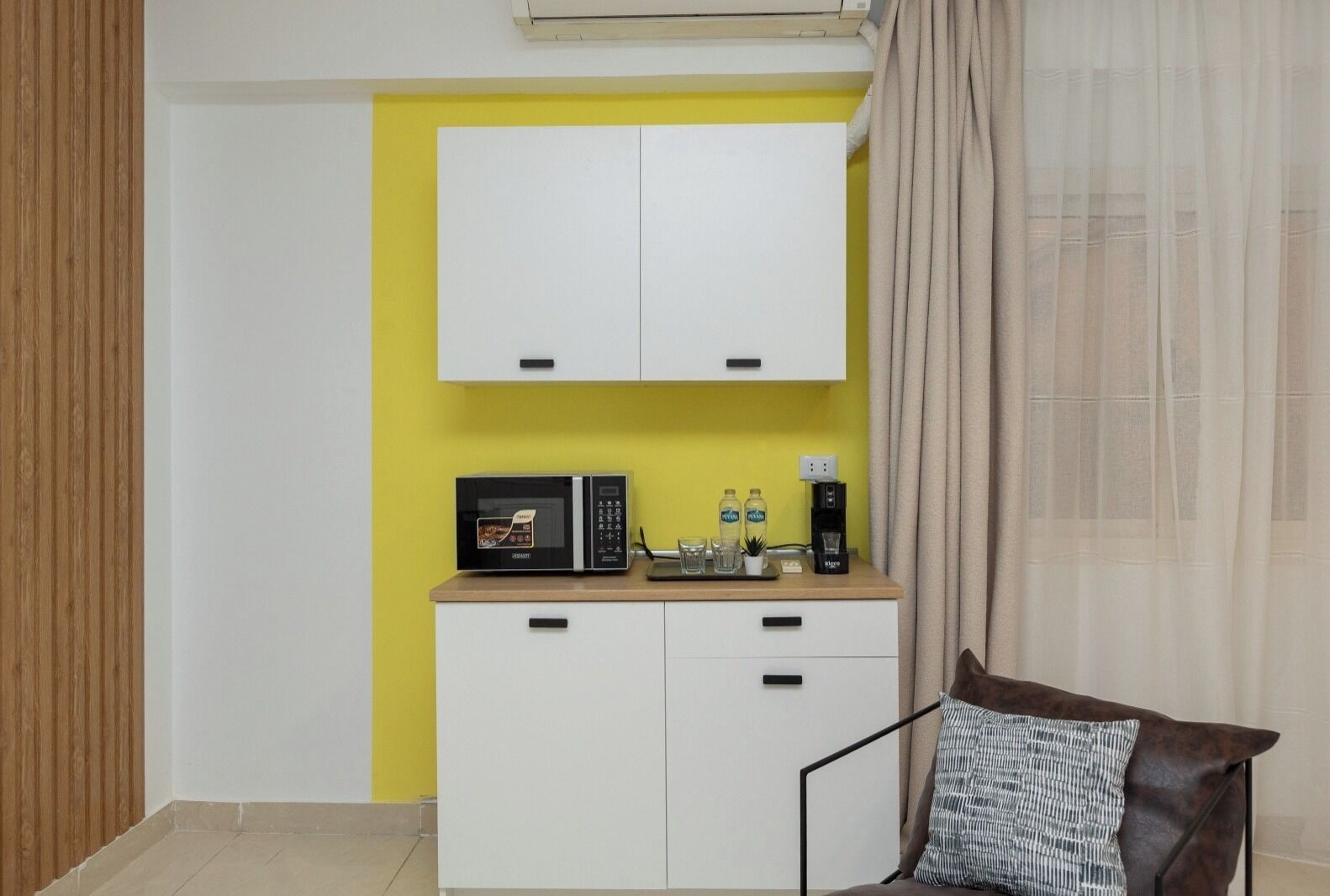 A compact living space with a kitchenette, including a microwave, coffee maker, and storage cabinets.