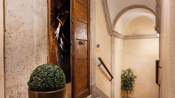 A hallway with a wooden door, a potted plant, and a staircase leading to an upper level. - Navona to Stay (Rome)