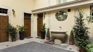A courtyard with a fountain, potted plants, and a stone floor. - Navona to Stay (Rome)