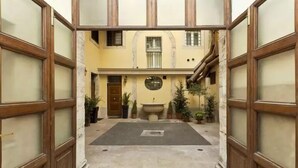 A courtyard with a central fountain, potted plants, and a door leading to a building. - Navona to Stay (Rome)